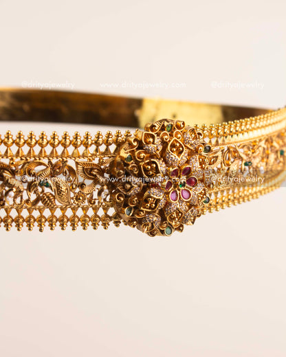 Handcrafted floral centerpiece of vadanam featuring ruby and emerald stones in antique gold finish.