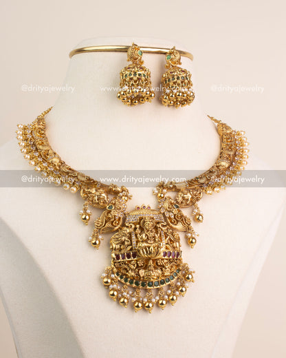 Antique gold short necklace with Lakshmi Devi pendant, ruby and emerald stones, and matching jhumkas.