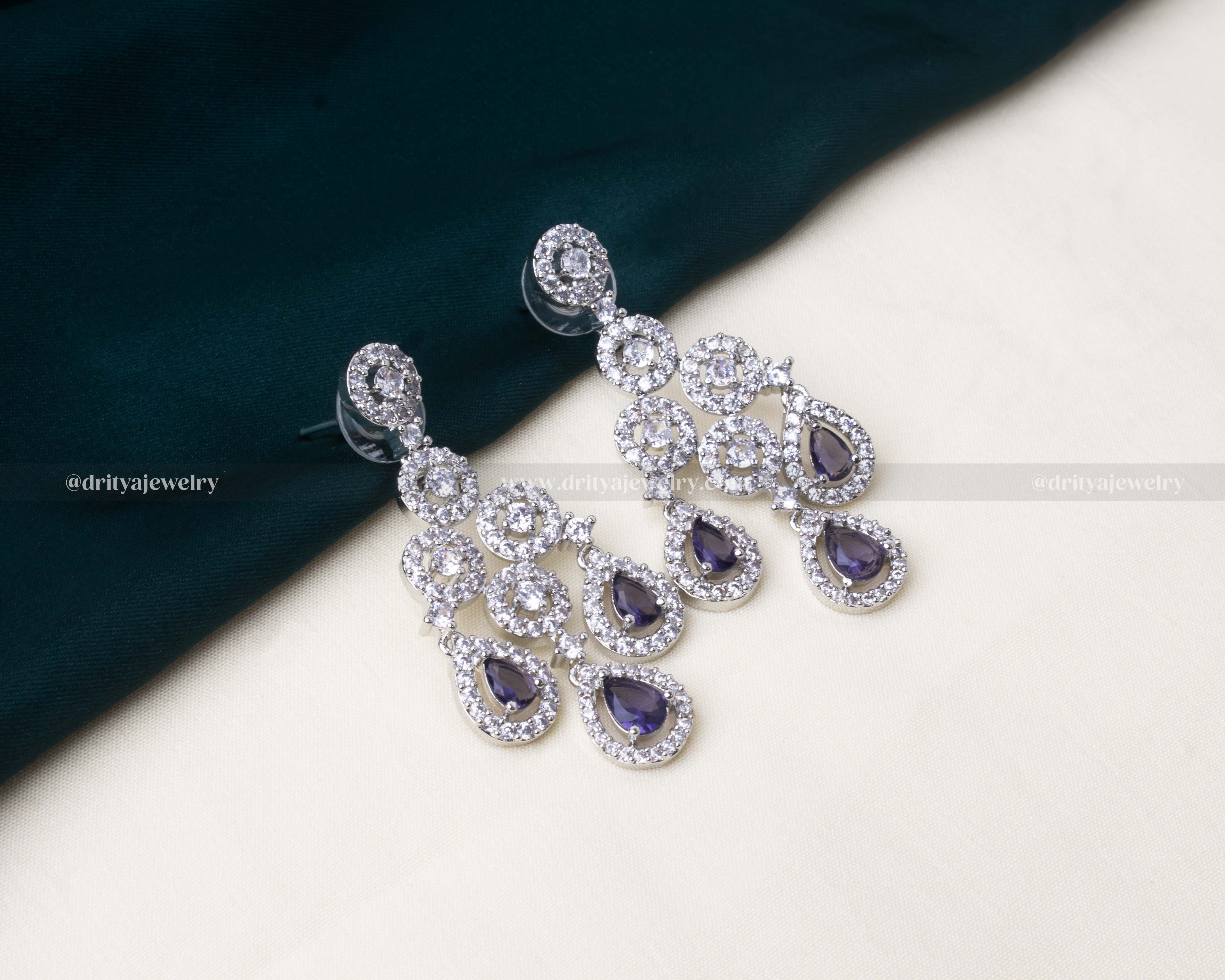 Elegant zircon choker necklace set with American diamonds, cascading teardrop design, paired with dangler earrings and a maang tikka in white and purple colors.