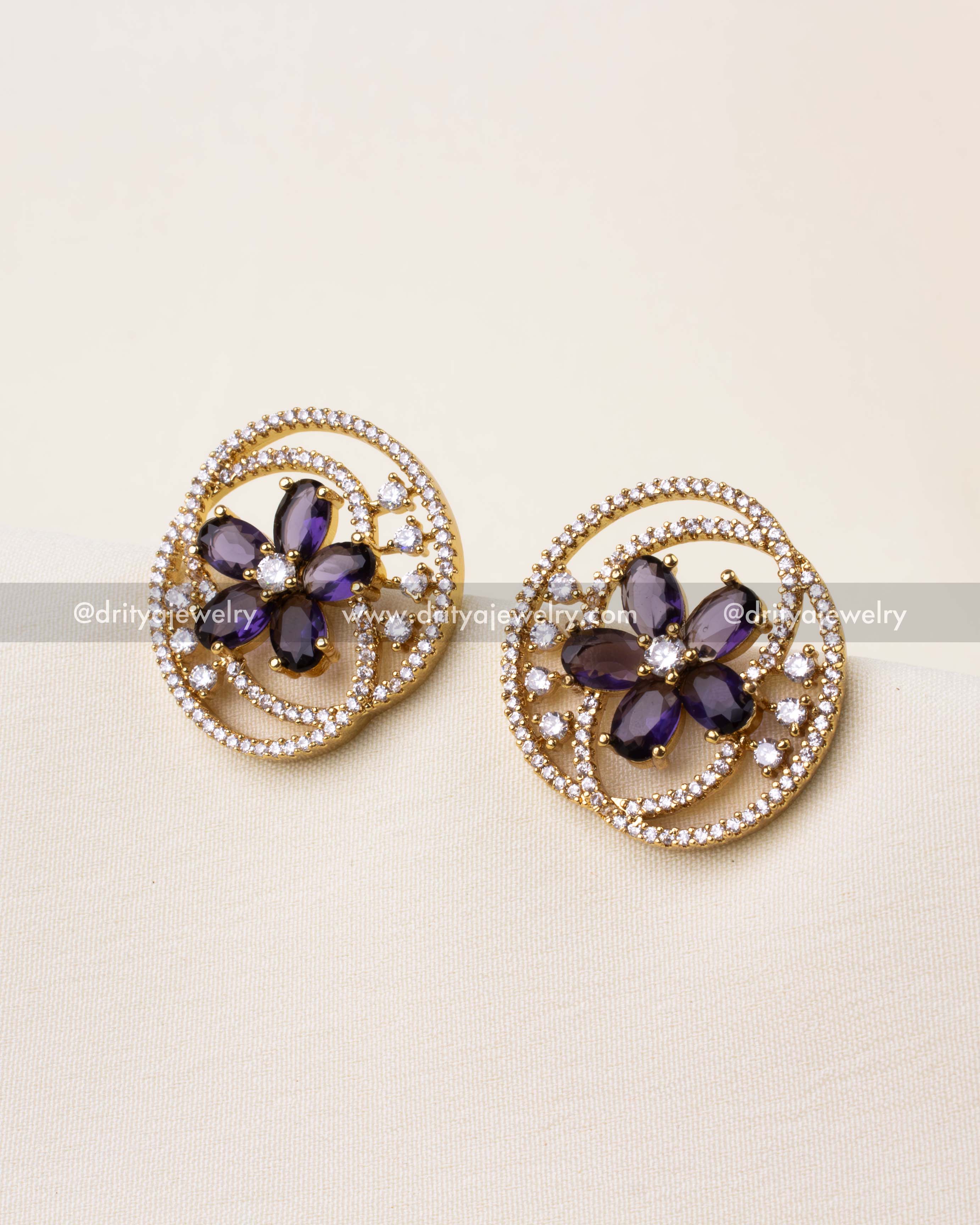 Gold-finished stud earrings with purple floral center and white CZ spiral detailing.