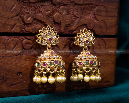 Opulent gold jhumka earrings with ruby and emerald accents and pearl details, ideal for bridal and festive wear.