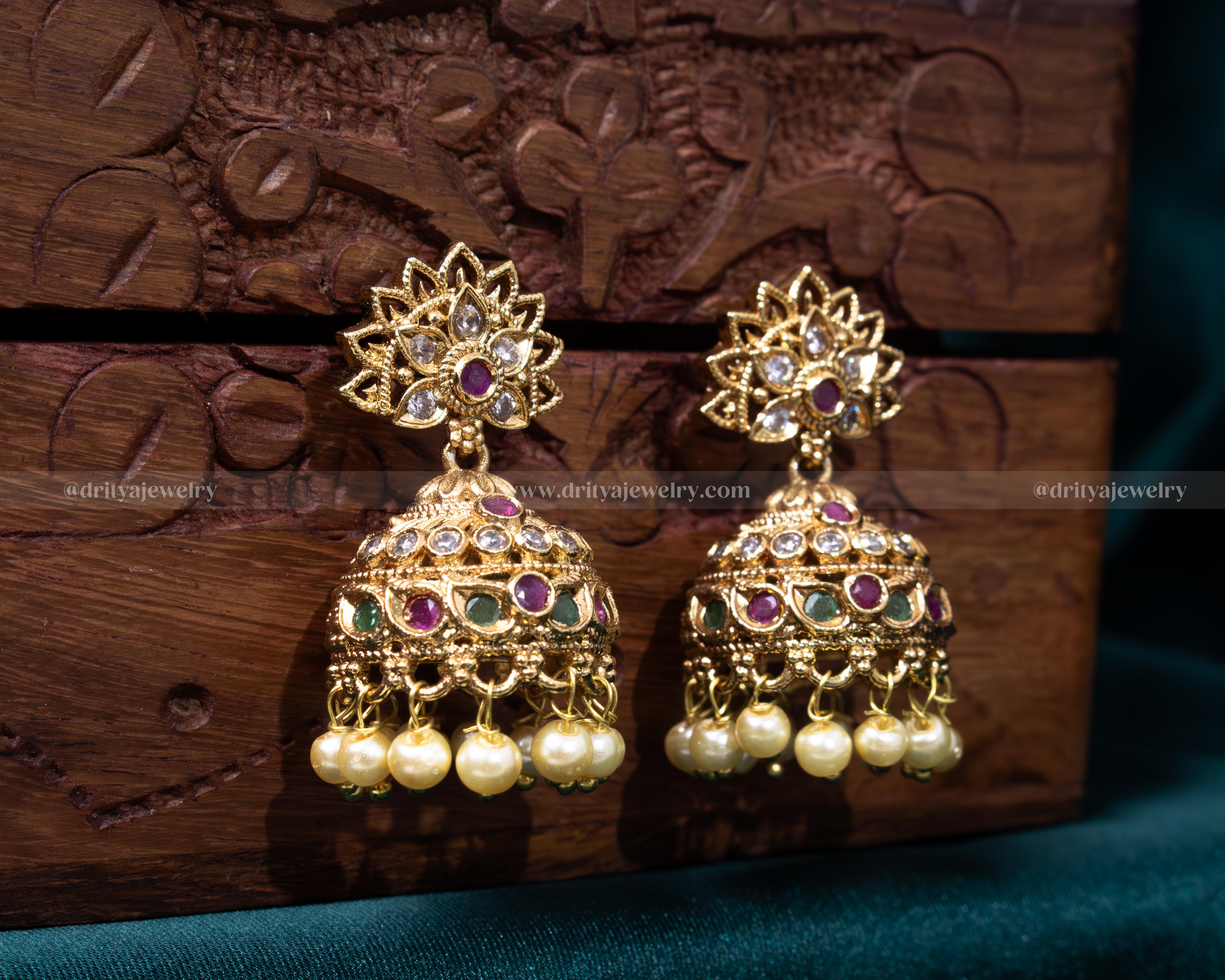 Opulent gold jhumka earrings with ruby and emerald accents and pearl details, ideal for bridal and festive wear.