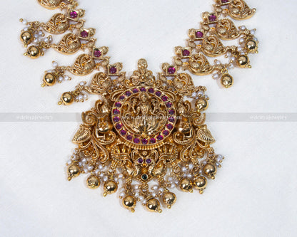 Exquisite gold-plated Haram necklace set featuring Lakshmi Devi motif surrounded by luminous Kundan stones and pearl embellishments.