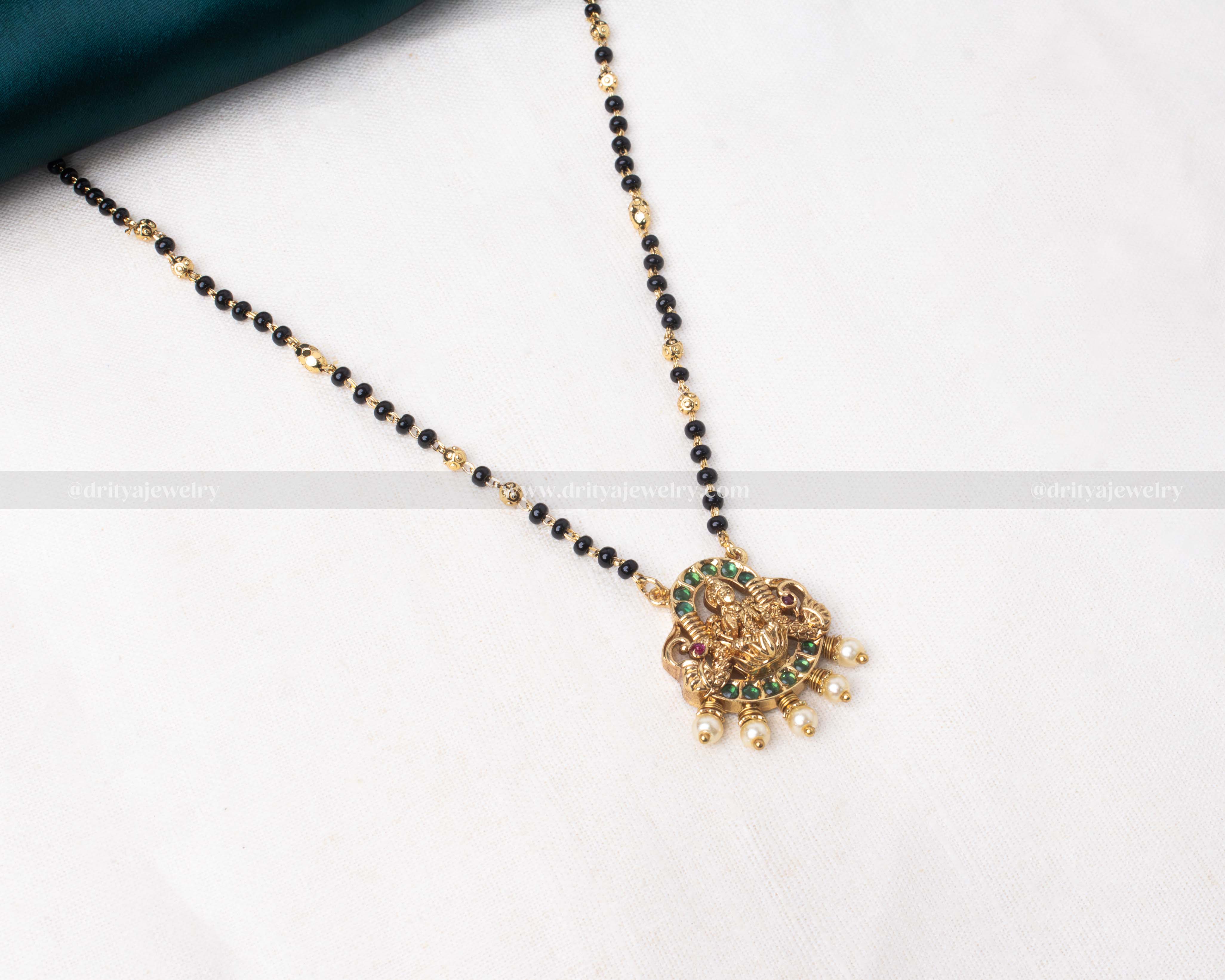 Gold polished black beads necklace featuring a green-toned Lakshmi Devi pendant with pearl accents, ideal for festive celebrations.