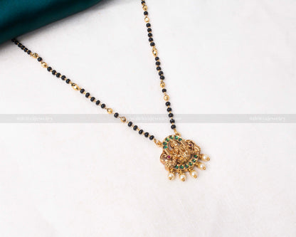 Gold polished black beads necklace featuring a green-toned Lakshmi Devi pendant with pearl accents, ideal for festive celebrations.