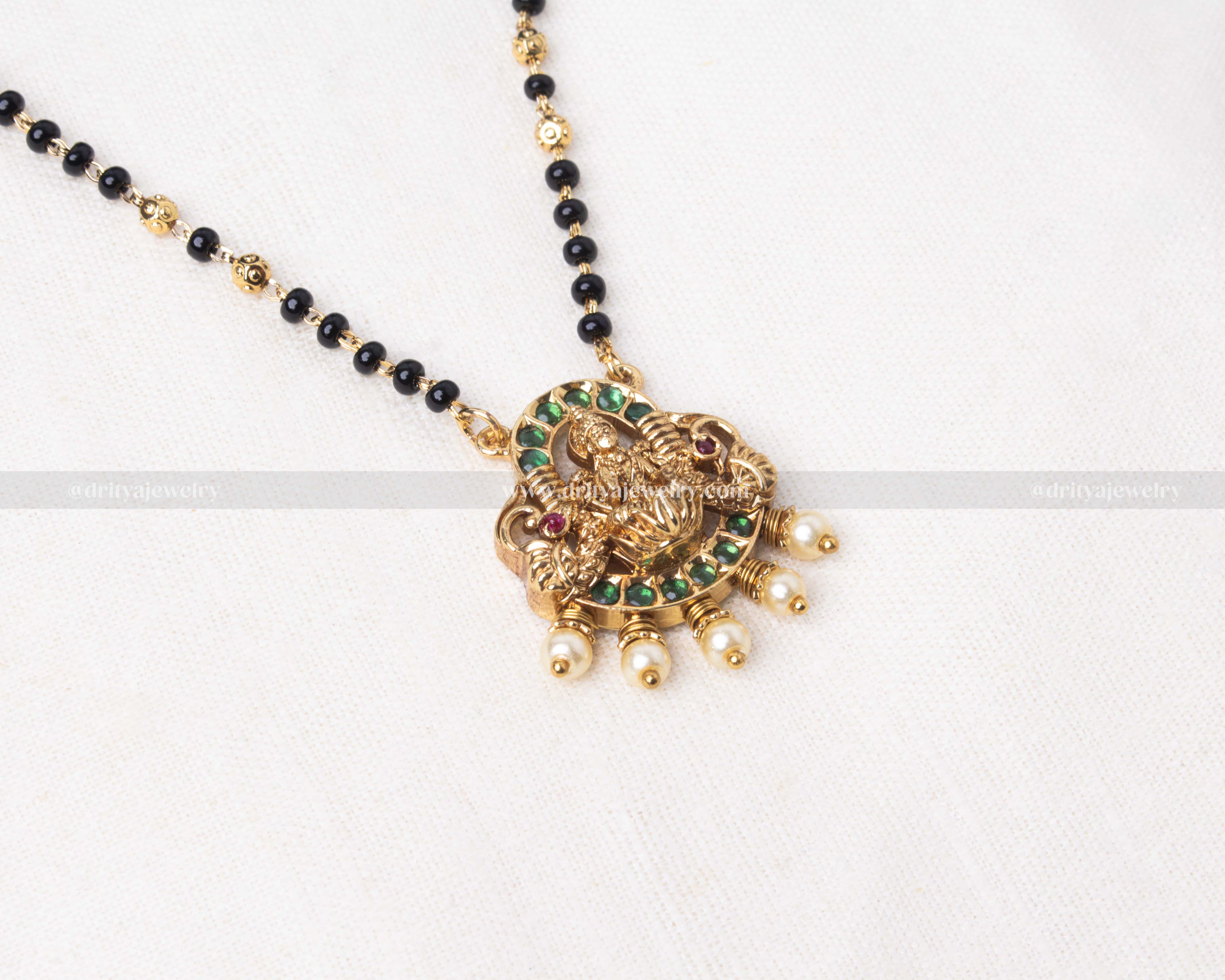 Gold polished black beads necklace featuring a green-toned Lakshmi Devi pendant with pearl accents, ideal for festive celebrations.