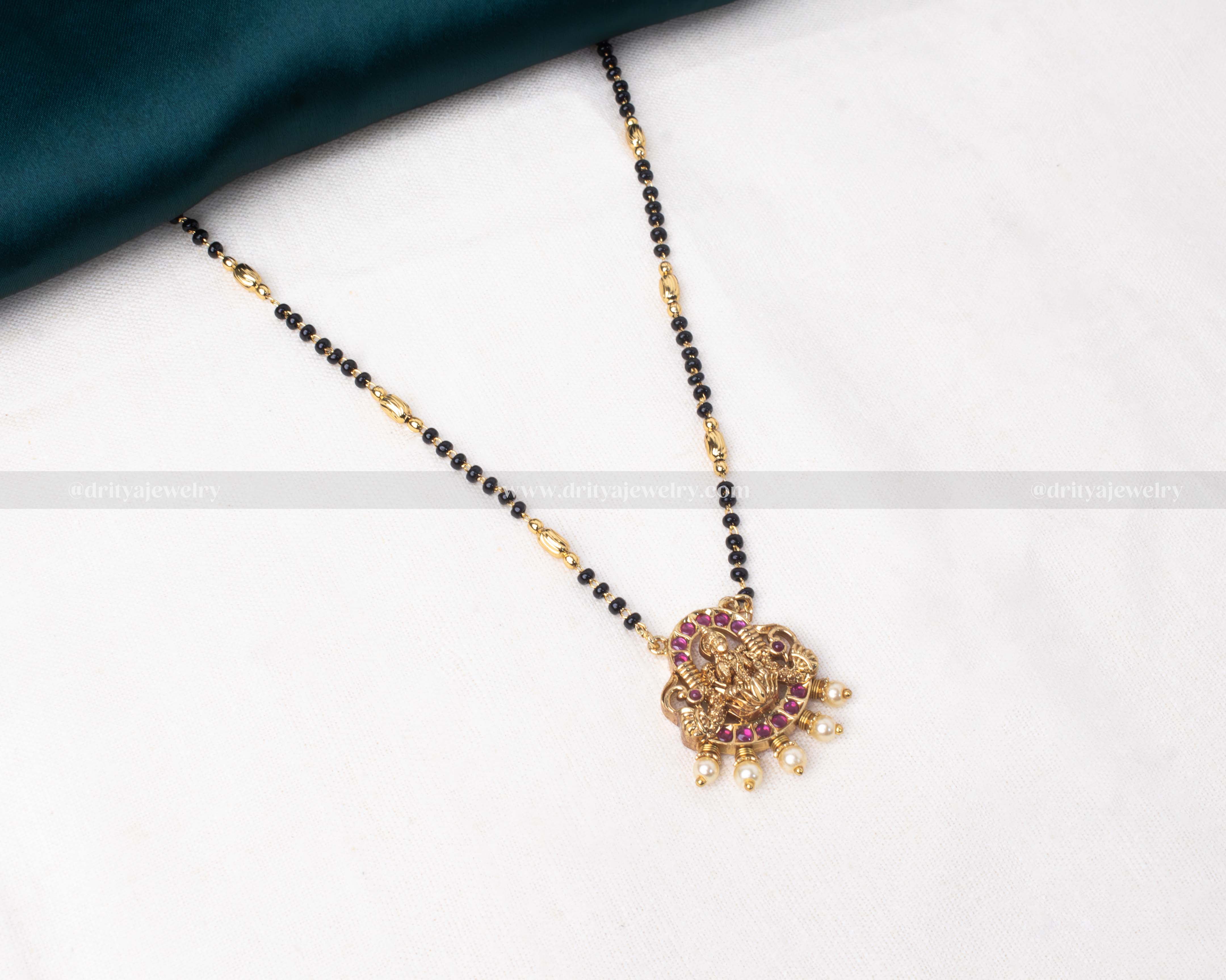 Gold polished black beads necklace featuring a red-toned Lakshmi Devi pendant with pearl accents, perfect for traditional occasions.