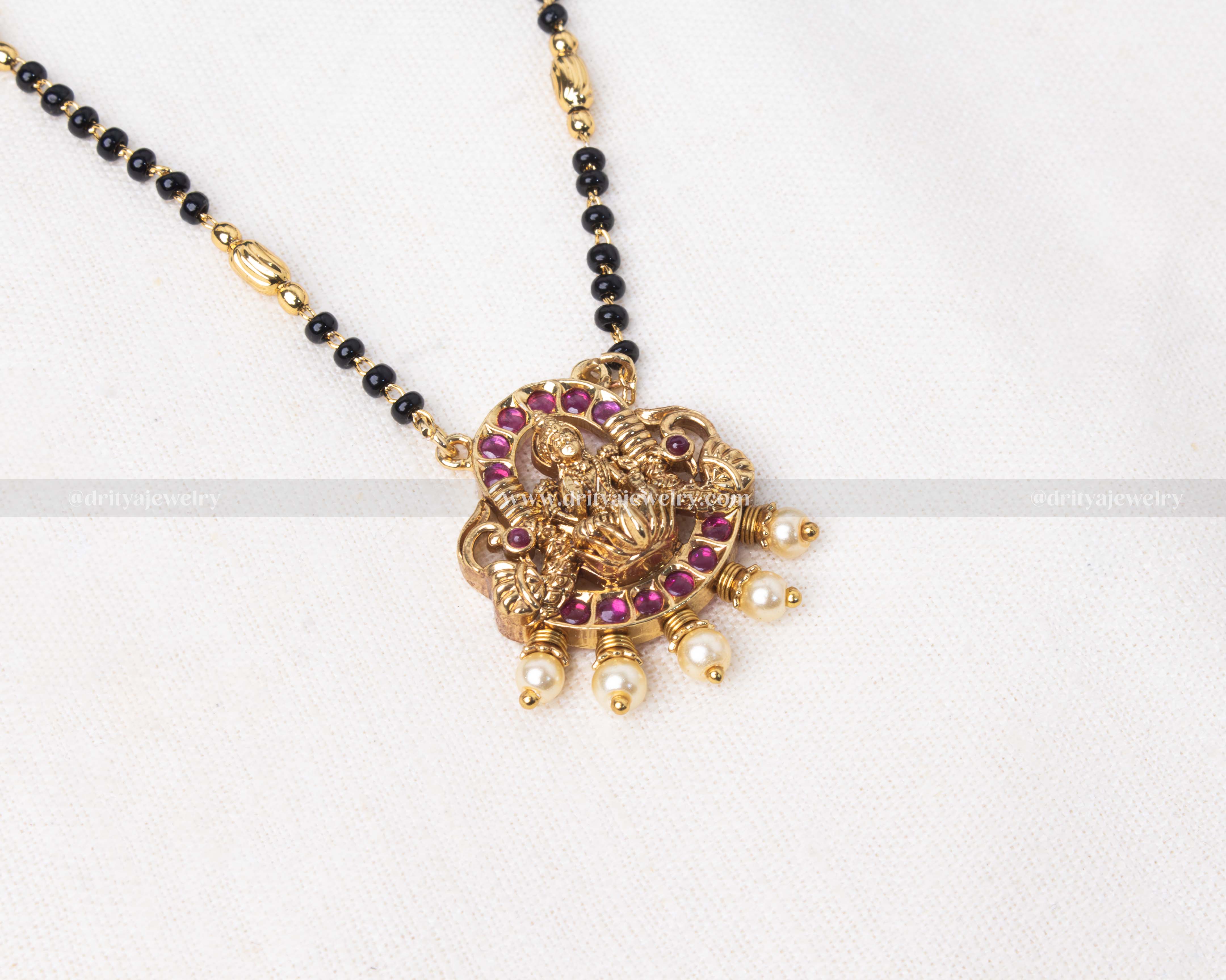 Gold polished black beads necklace featuring a red-toned Lakshmi Devi pendant with pearl accents, perfect for traditional occasions.