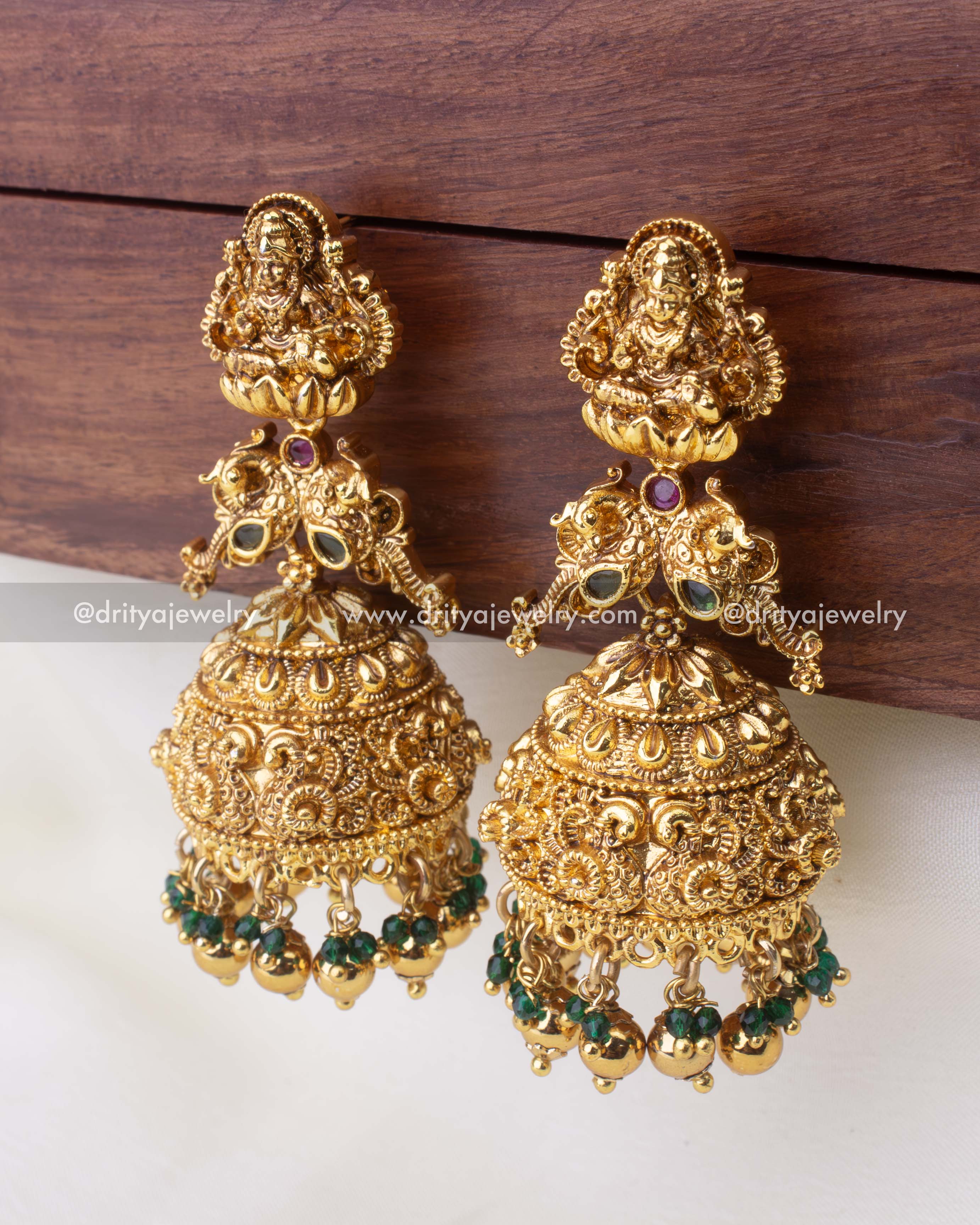 Oversized temple-style Jhumkas featuring Goddess Lakshmi and emerald bead drops.