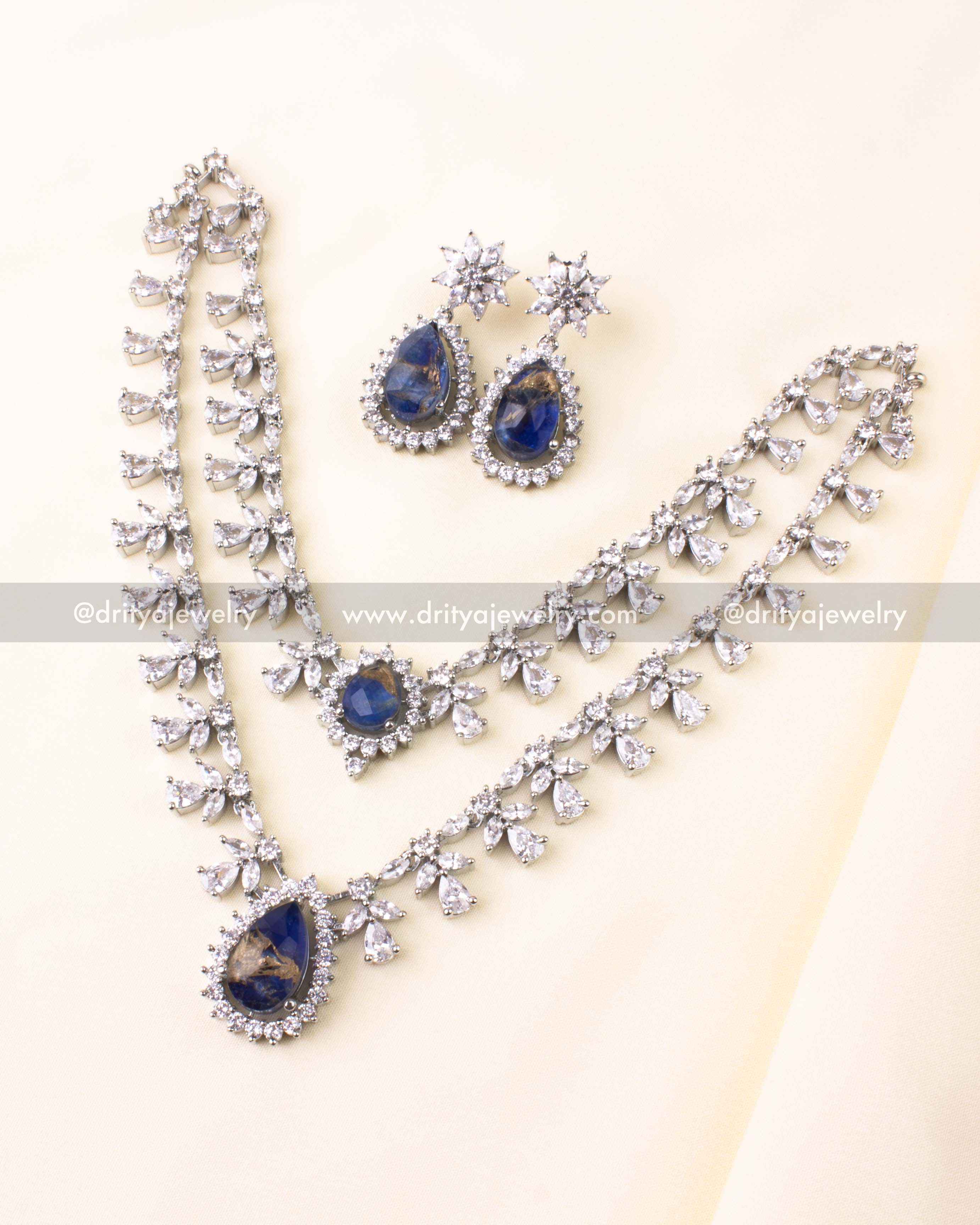 Silver-toned dual-layer necklace set with teardrop blue stone pendant and CZ embellishments.