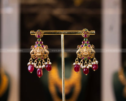 Matching gold-plated earrings from Dritya Jewelry’s temple necklace set, featuring ruby beads, emerald stones, and pearl drops for an elegant look.