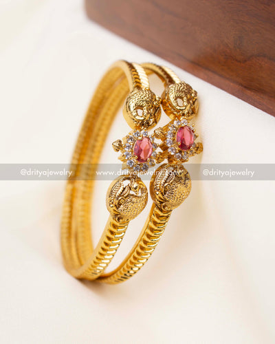 Pair of gold bangles with ruby red stone and intricate peacock carvings.