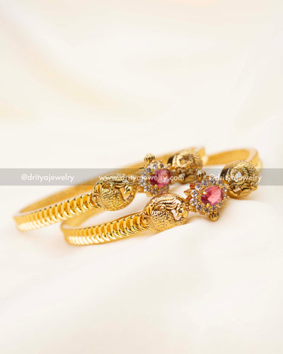 Pair of gold bangles with ruby red stone and intricate peacock carvings.