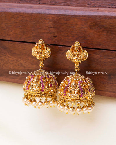 Dome-shaped jhumkas with ruby red stones, intricate carvings, and pearl drops.