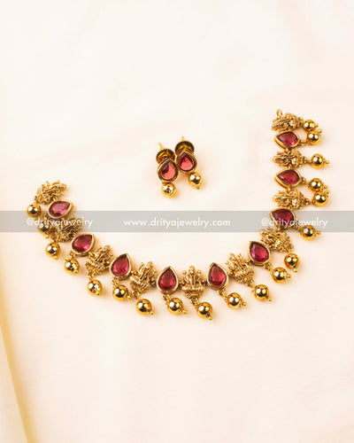 Traditional short necklace set with ruby red stones and goddess motifs in antique gold.