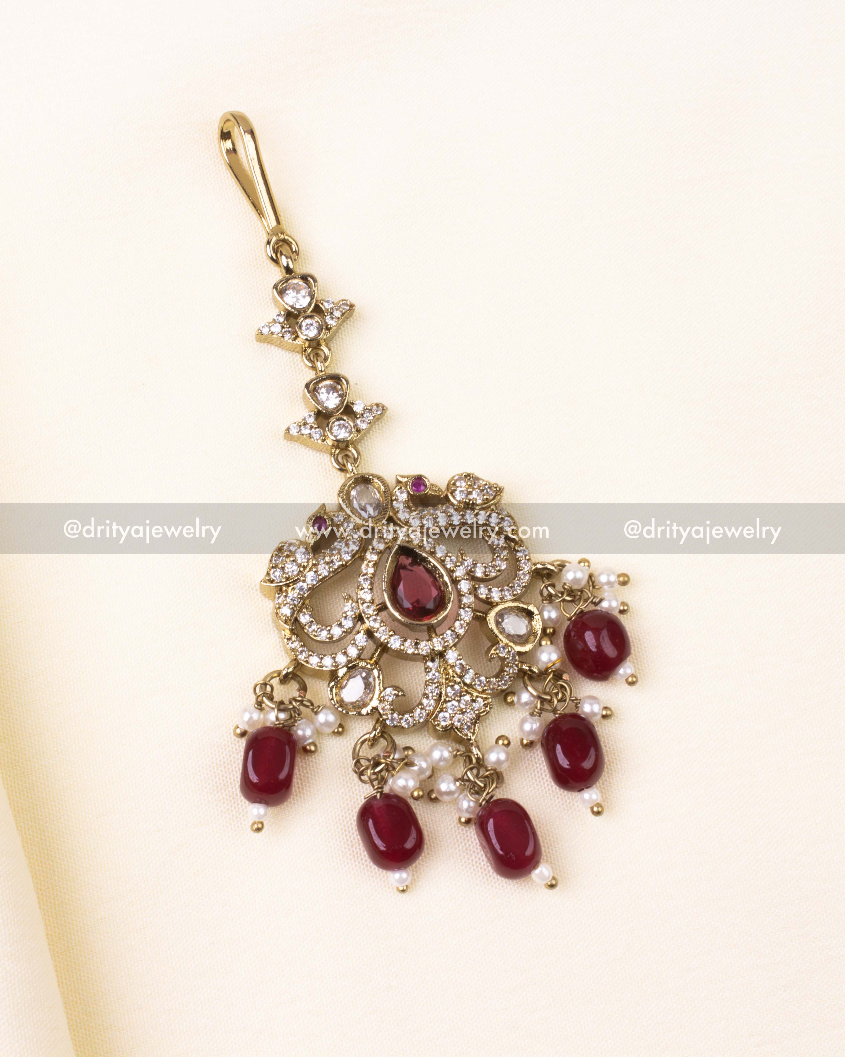 Victorian-style maang tikka with ruby red stones and pearl embellishments.