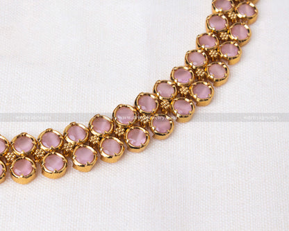 Close-up view of short necklace with blush pink stones set in gold-toned metal.