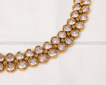 Close-up view of short necklace with white stones set in gold-toned metal.