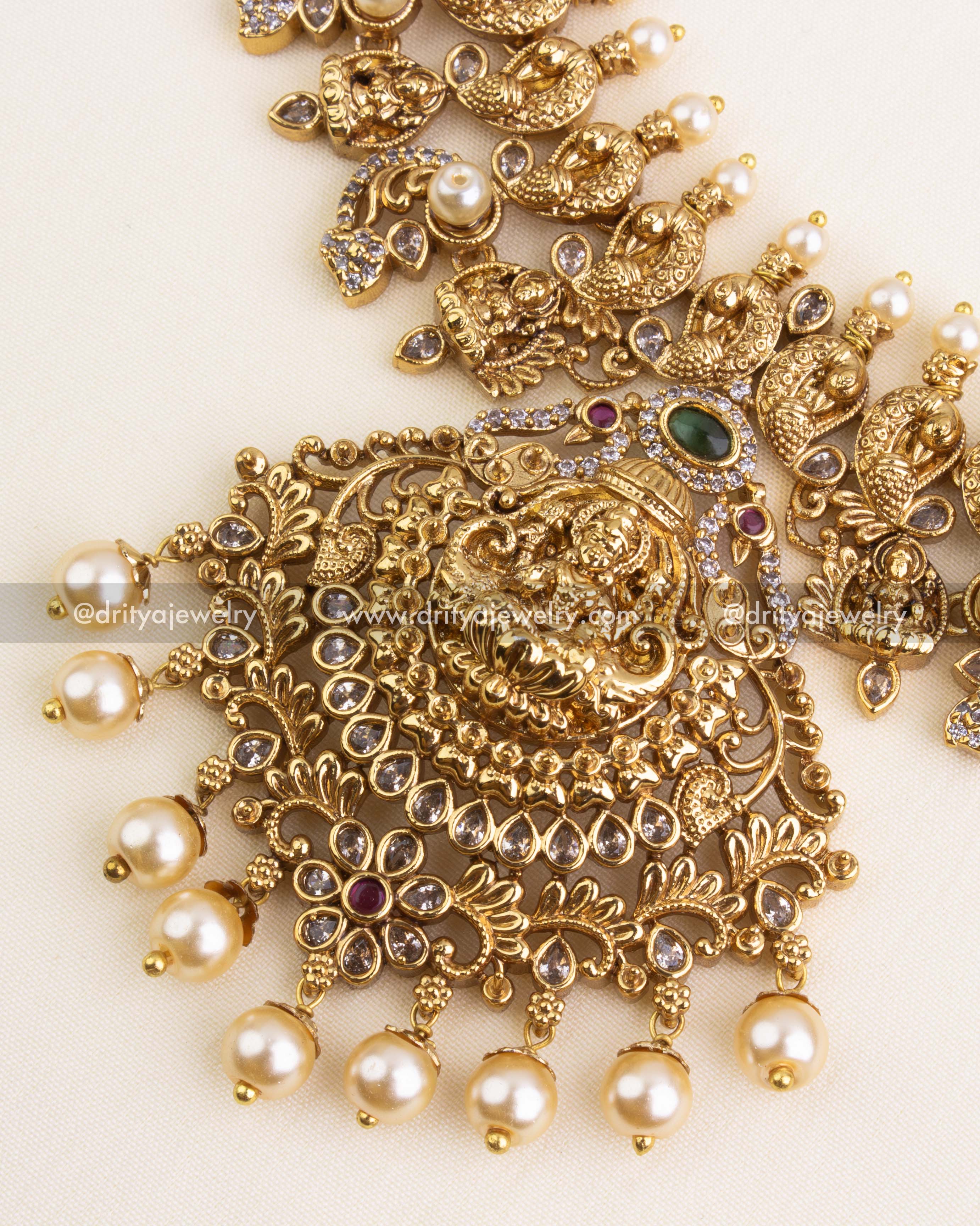 Close-up of grand Lakshmi Devi pendant with layered floral carvings, CZ stones, and pearl drops in antique gold polish.