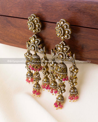 Close-up view of antique gold earrings with multi-layered jhumka design and pink bead drops.