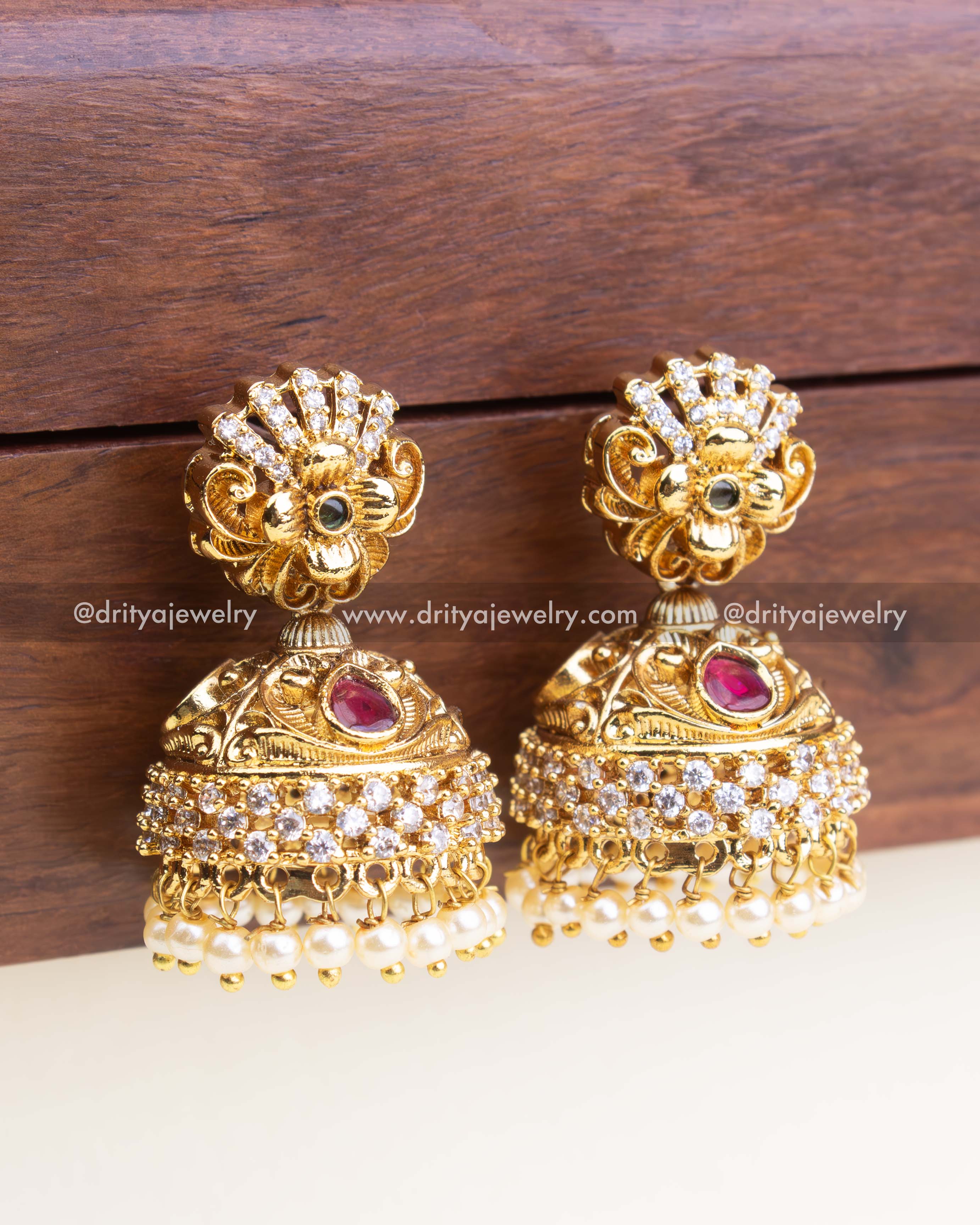 Intricate temple-style jhumka with layered CZ and pearl detailing in antique gold finish.