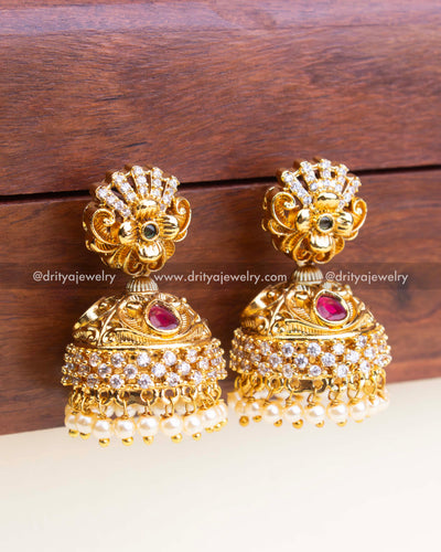 Intricate temple-style jhumka with layered CZ and pearl detailing in antique gold finish.