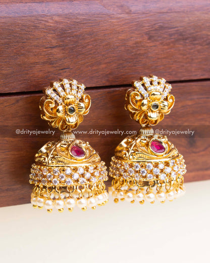 Intricate temple-style jhumka with layered CZ and pearl detailing in antique gold finish.