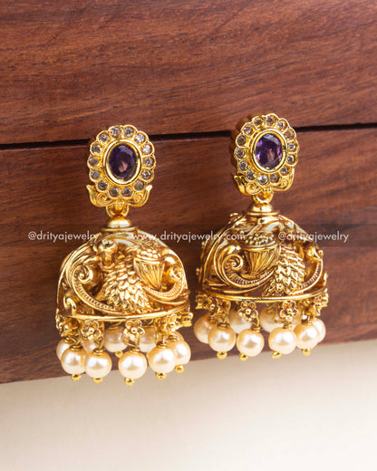 Temple-style jhumka with embossed peacock detailing, pearl clusters, and oval purple stone stud.