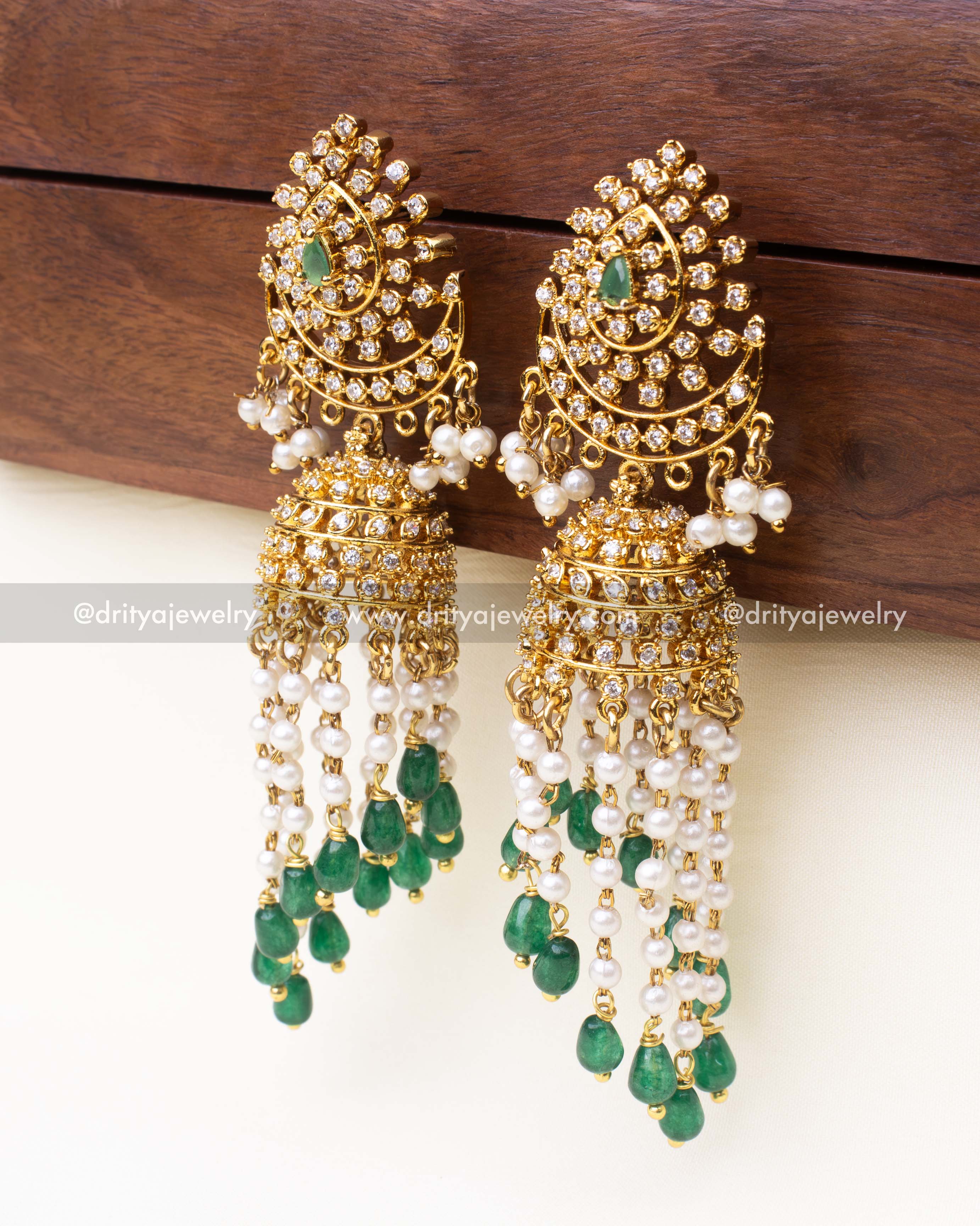 Side profile of emerald green Jhumka earrings with layered pearl strands and gold finish.