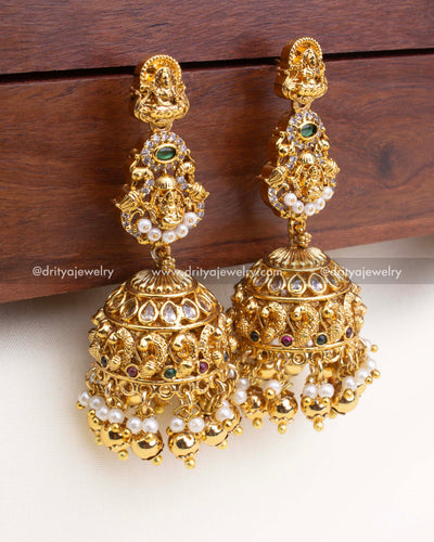 Antique-finish jhumka earrings with Lakshmi Devi design, peacock dome, and pearl-gold ball drops.