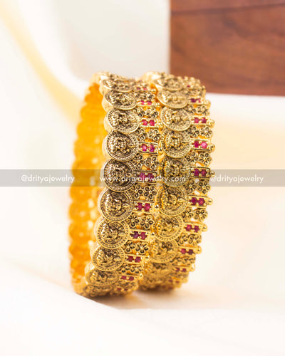 A pair of antique gold Nakshi bangles with ruby red stones and traditional coin motifs.