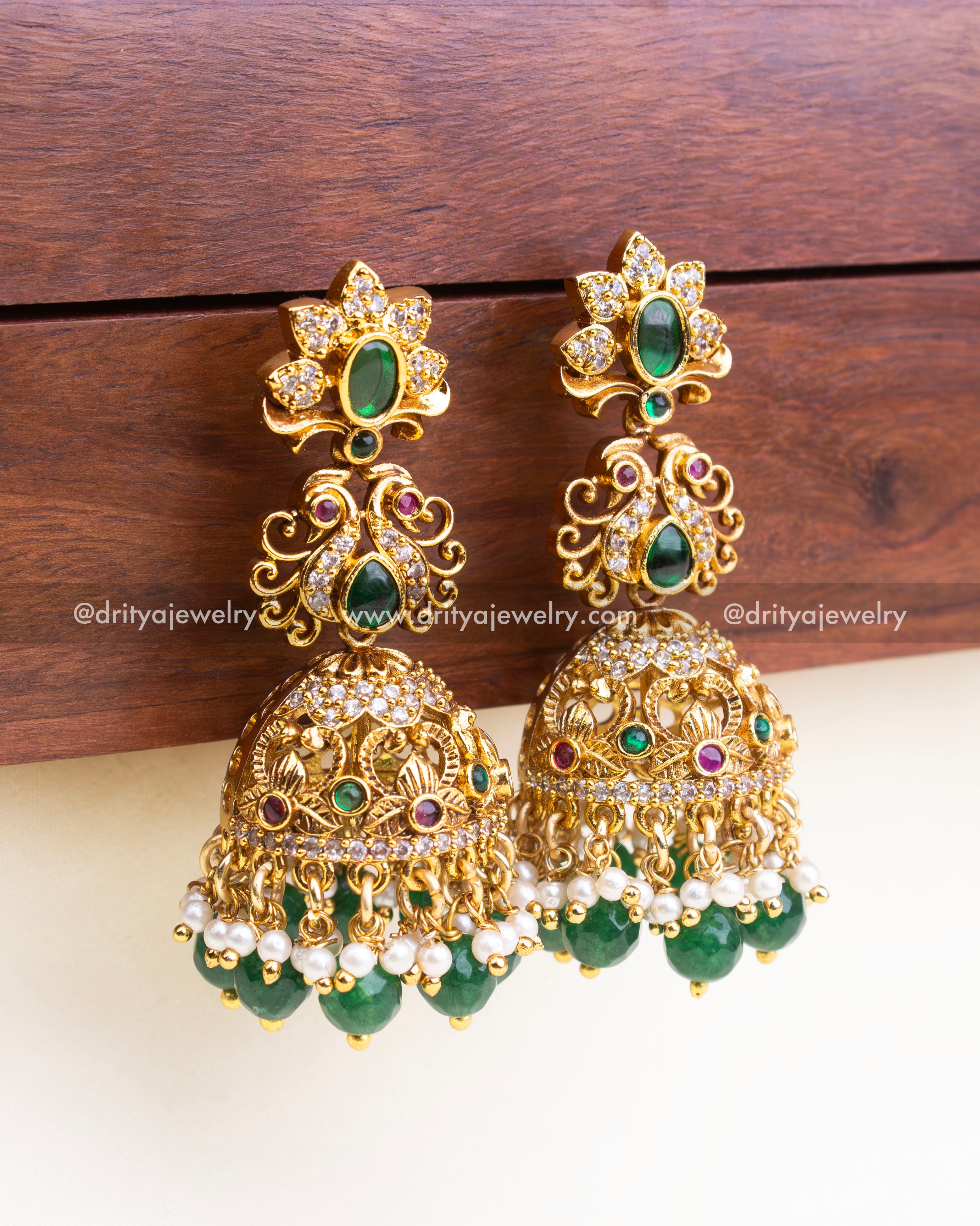 Detailed side view of ornate antique gold jhumka earrings with CZ, green stones, and pearl bead hangings.
