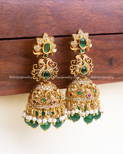 Detailed side view of ornate antique gold jhumka earrings with CZ, green stones, and pearl bead hangings.