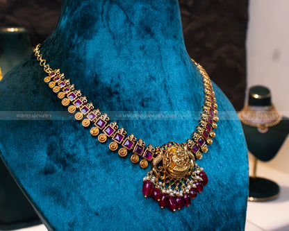 Dritya Jewelry’s gold-plated temple necklace set featuring a Lakshmi pendant with ruby beads, pearl accents, and intricate gold details, perfect for weddings and festive occasions.