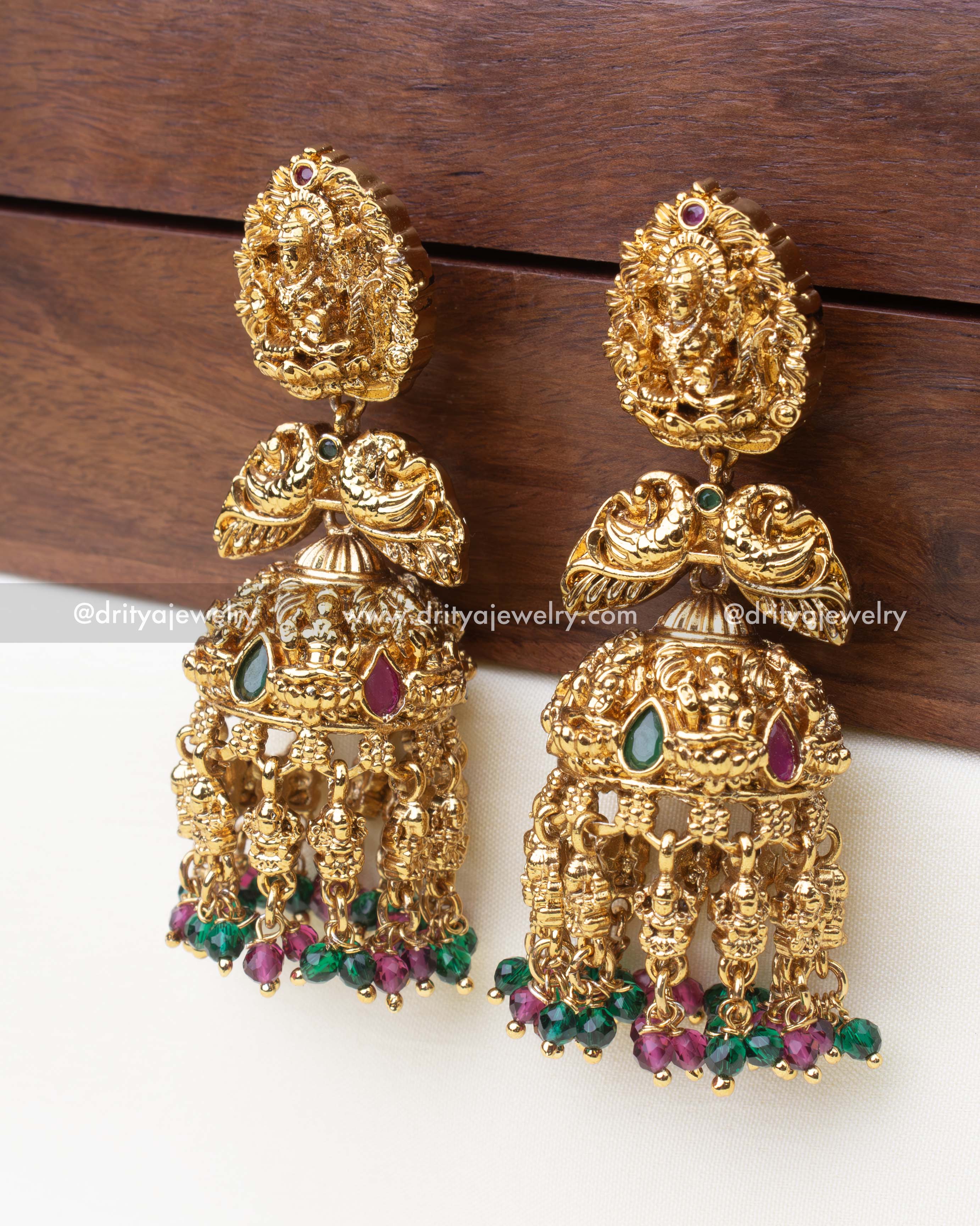Close-up view of intricately carved temple-style jhumkas with green and magenta beaded drops.