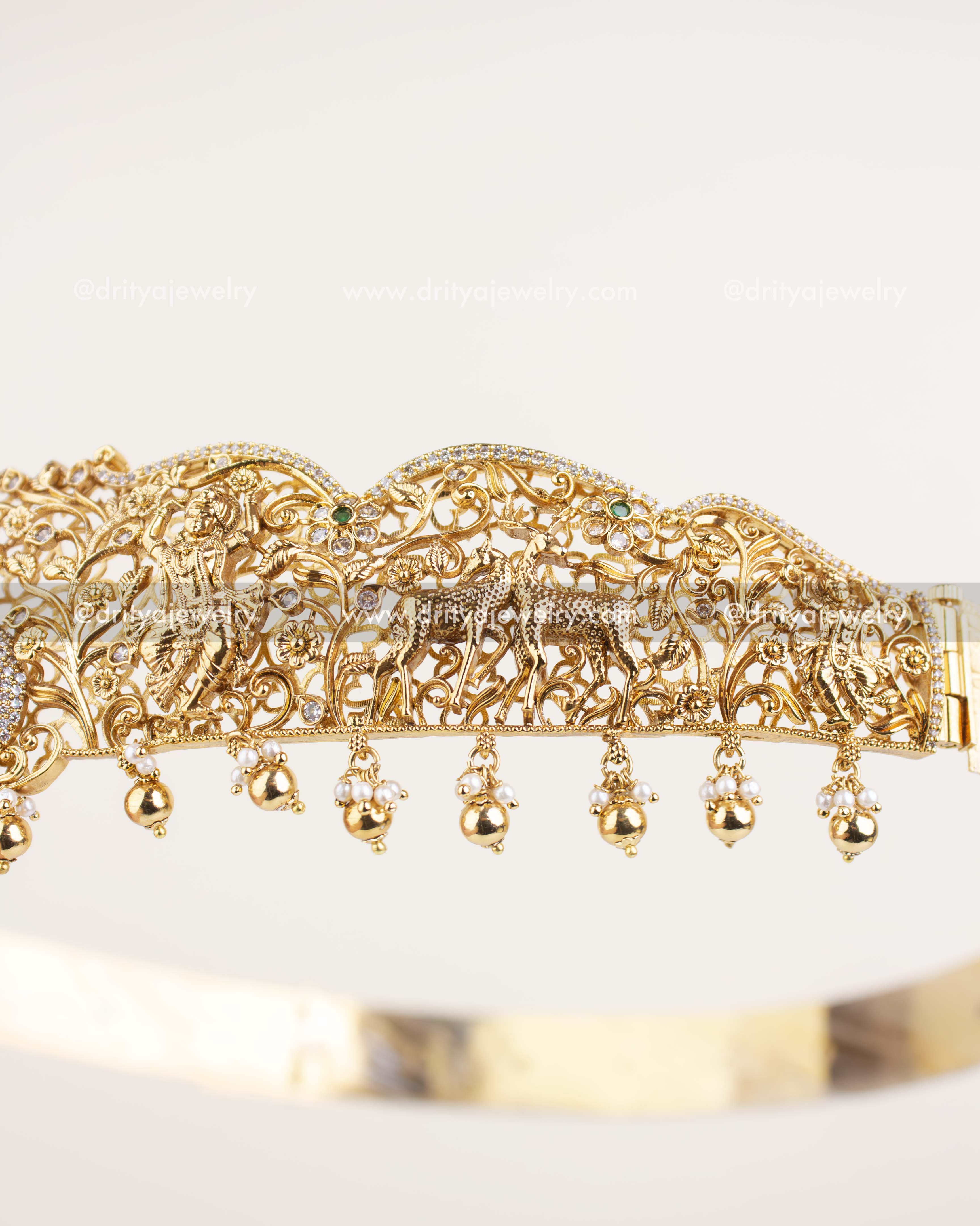 Peacock and forest detailing on gold temple vadanam with CZ and green stones.