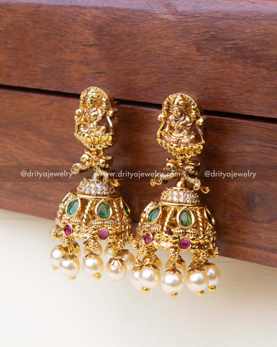Small temple Jhumka earrings featuring a detailed goddess carving, green and ruby stones, and pearl drops.