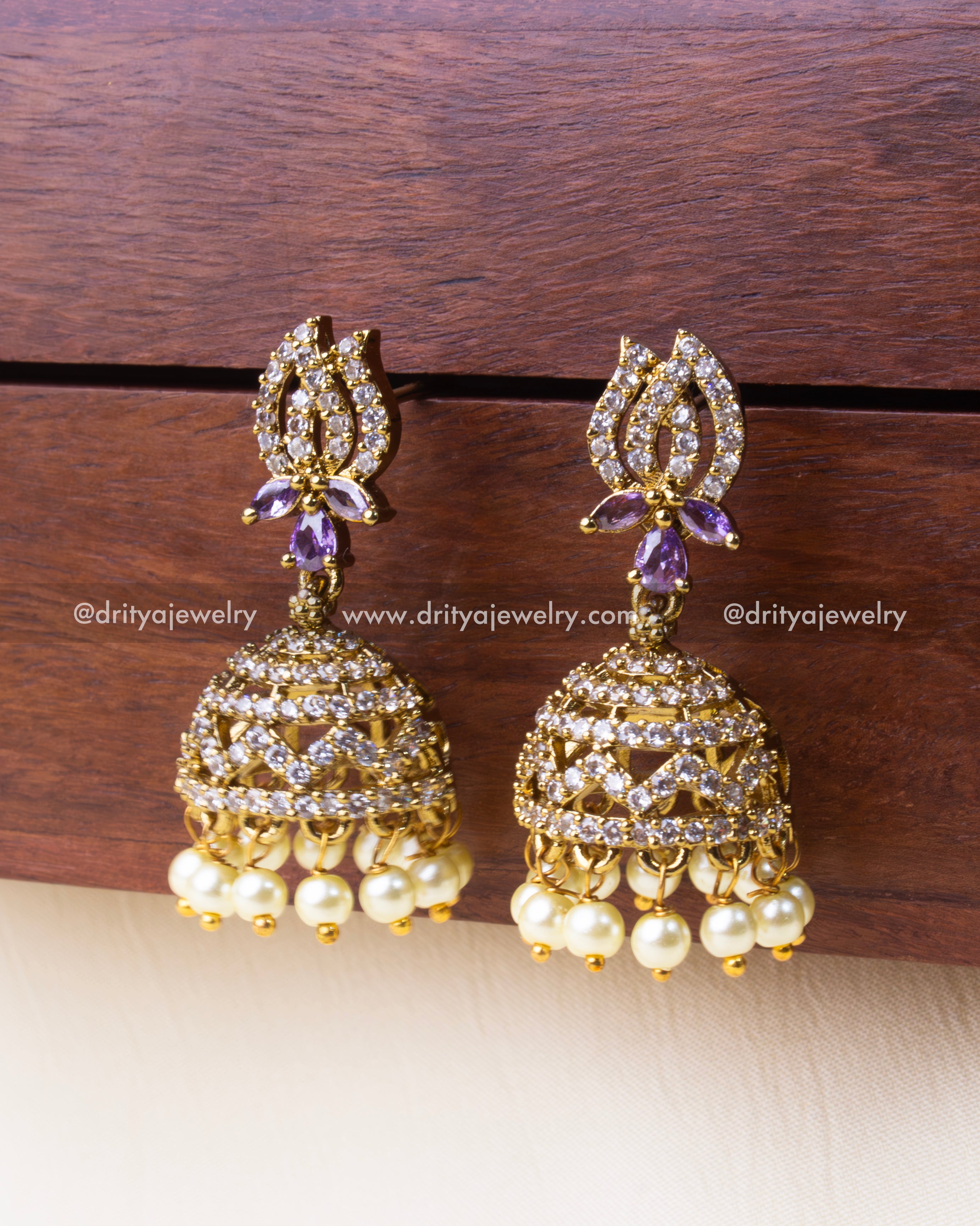Small-sized gold-plated jhumka earrings featuring CZ stone detailing, a purple centerpiece, and dangling pearl drops.