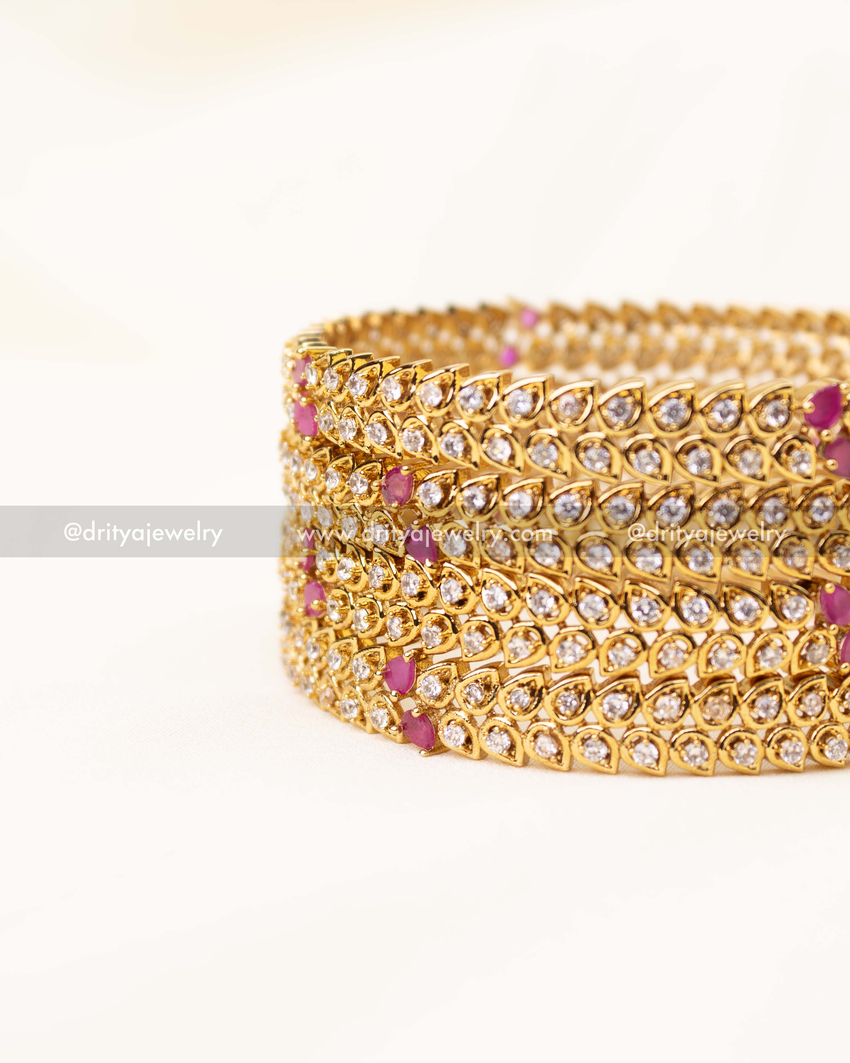 Set of gold-plated CZ bangles with tear-drop stones and pink accents.