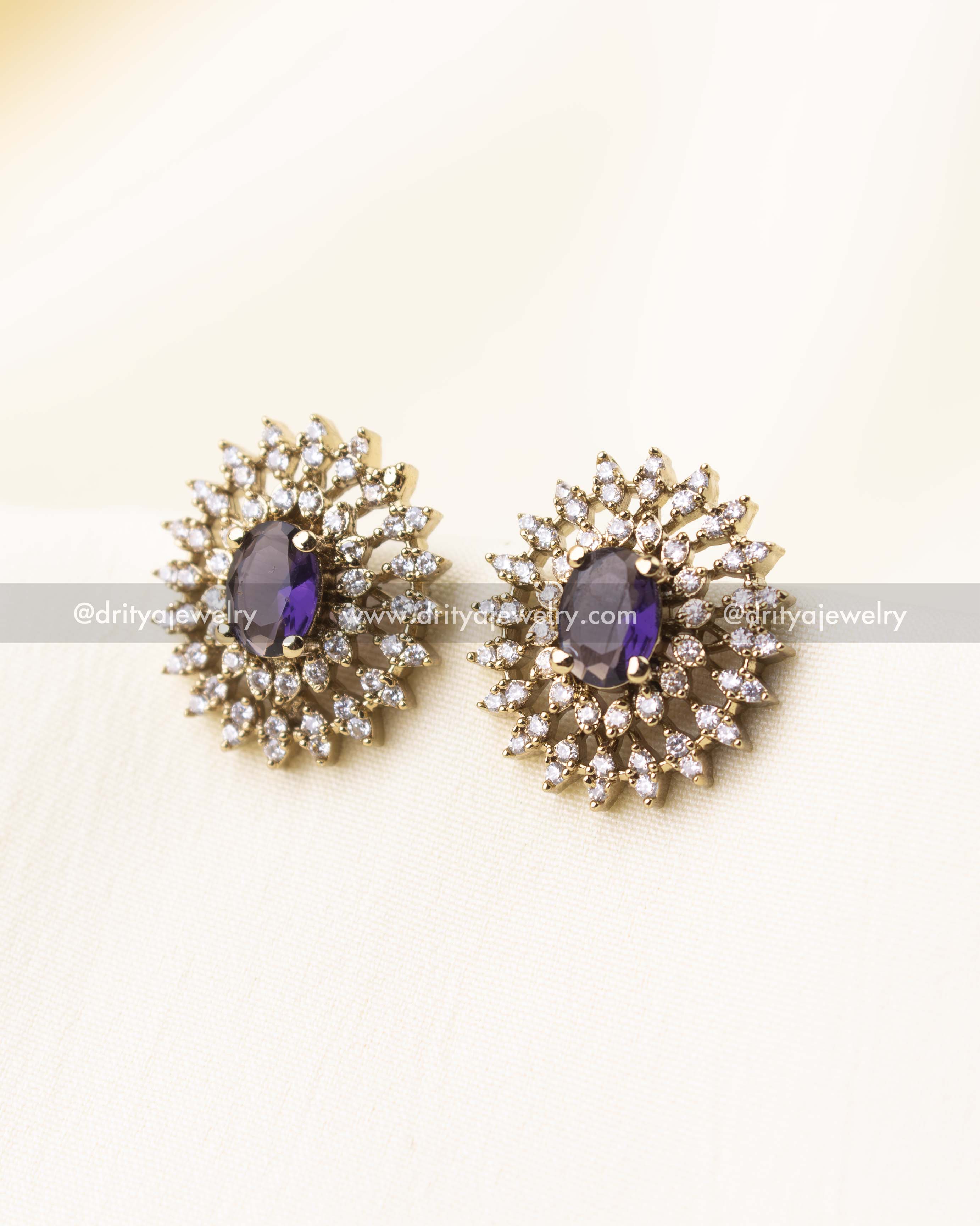 Matching stud earrings with a central purple gem surrounded by multiple layers of shimmering CZ stones.
