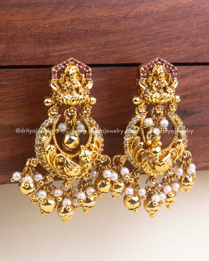 Intricate Lakshmi and peacock design chandbali earrings with gold polish and pearl drops.
