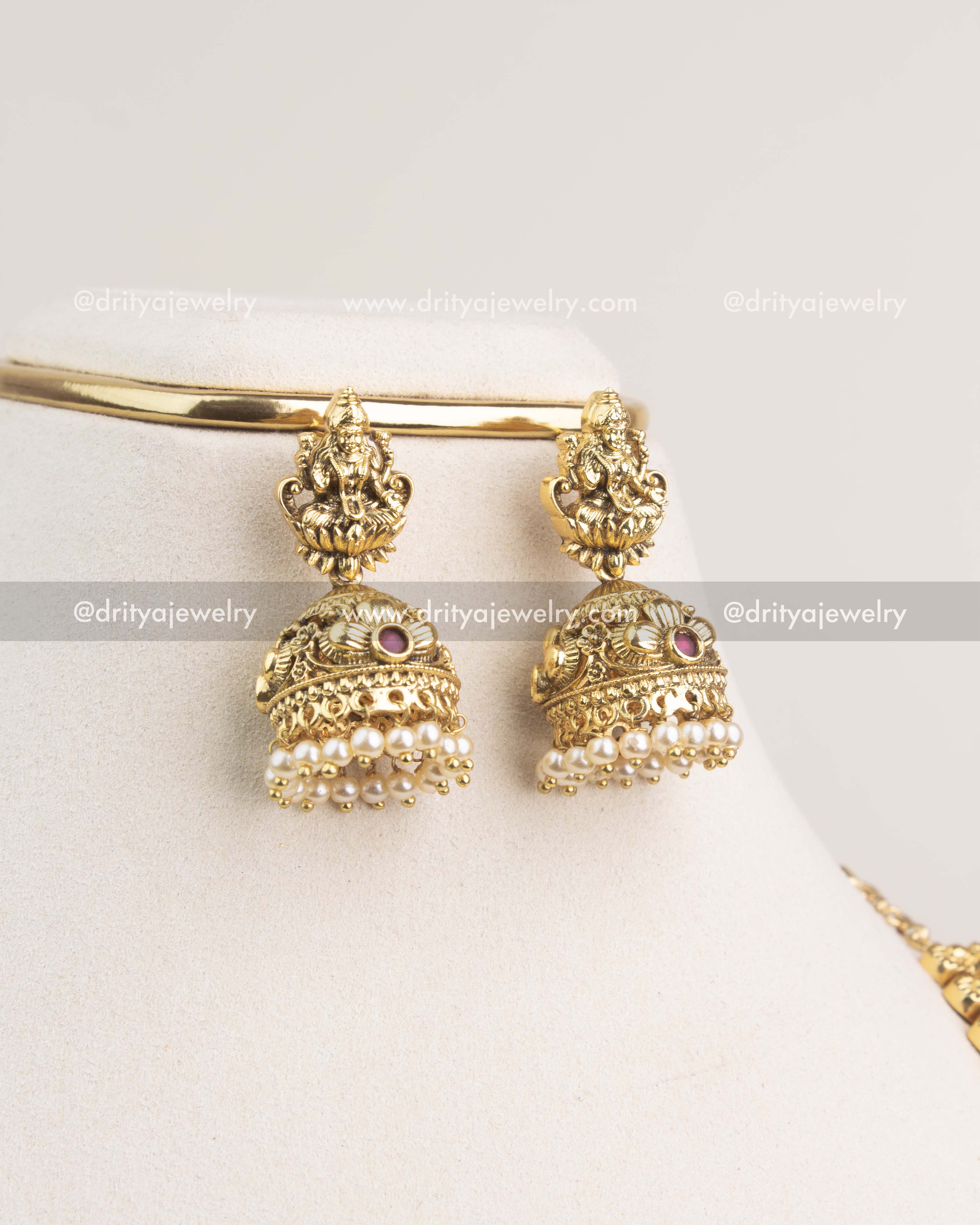 Gold jhumka earrings with Lakshmi motifs and pearl clusters in antique finish.