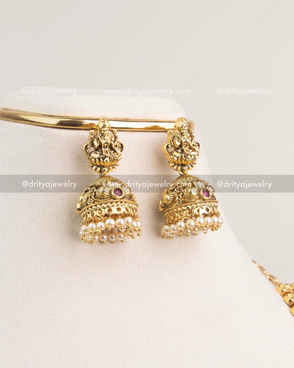 Gold jhumka earrings with Lakshmi motifs and pearl clusters in antique finish.