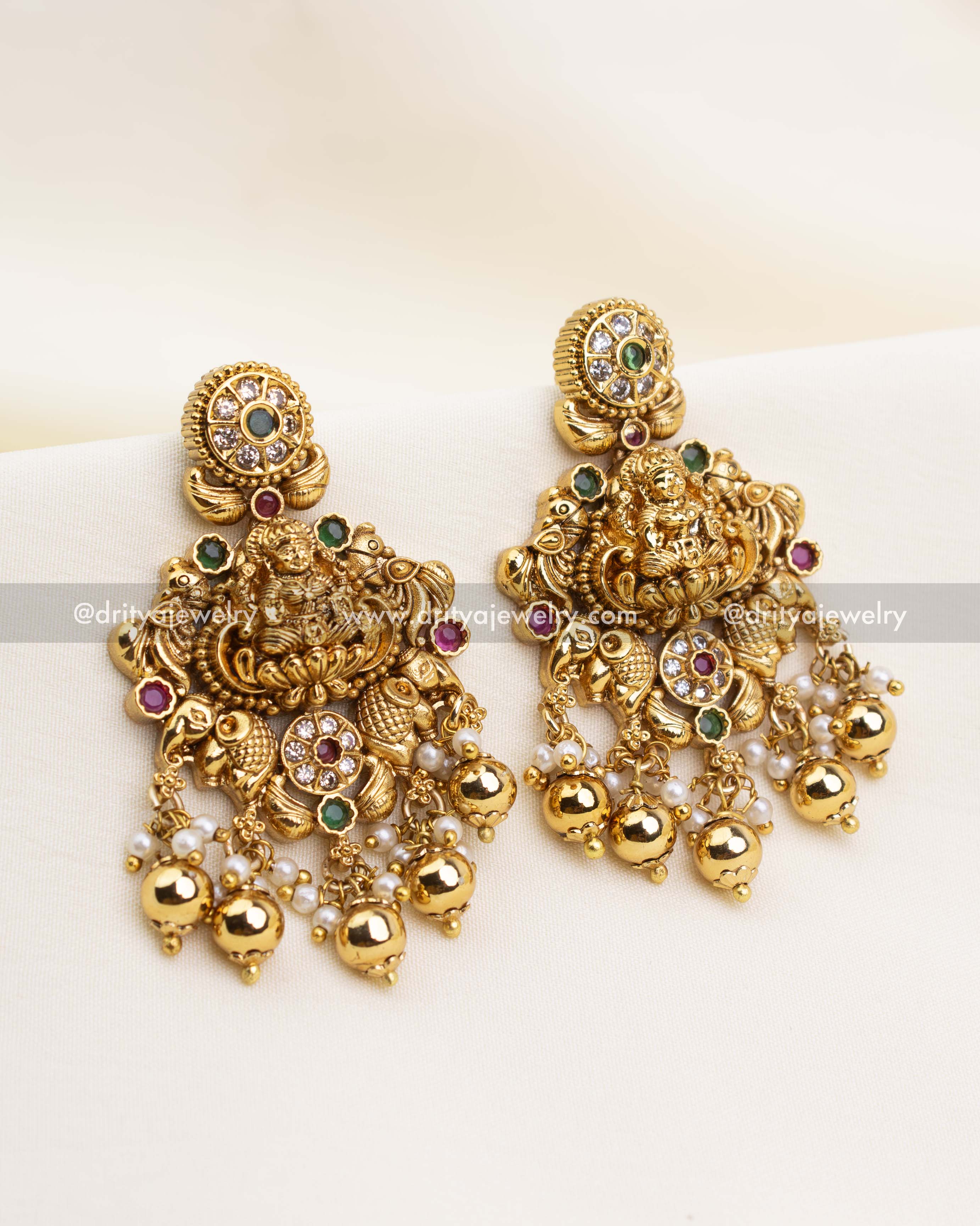 Gold-plated earrings featuring goddess motif, peacock detailing, and golden ball and pearl drops to match the Nakshi short necklace.