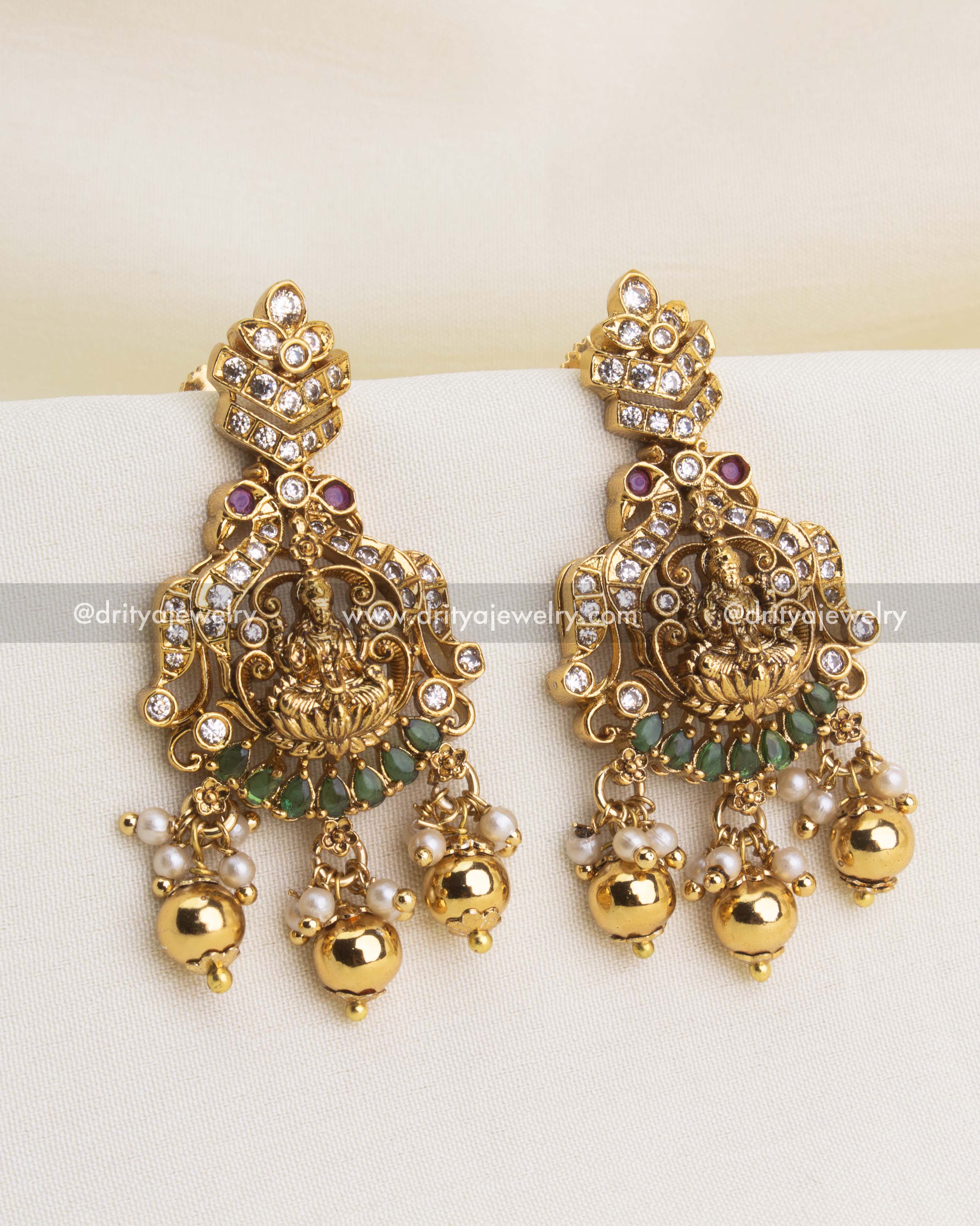 Traditional temple earrings with Lakshmi carving, CZ highlights, green stones, and pearl clusters.