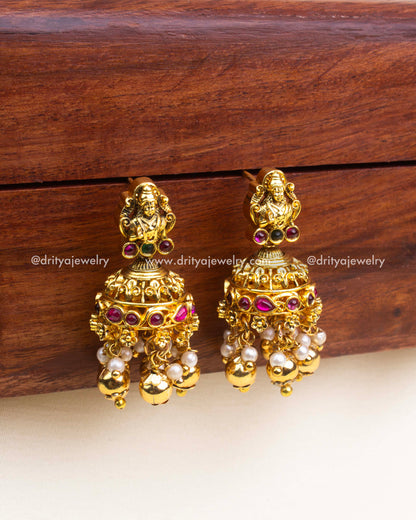 Gold temple jhumka earrings with deity top, kemp inlay and pearl–ball danglers in antique finish.