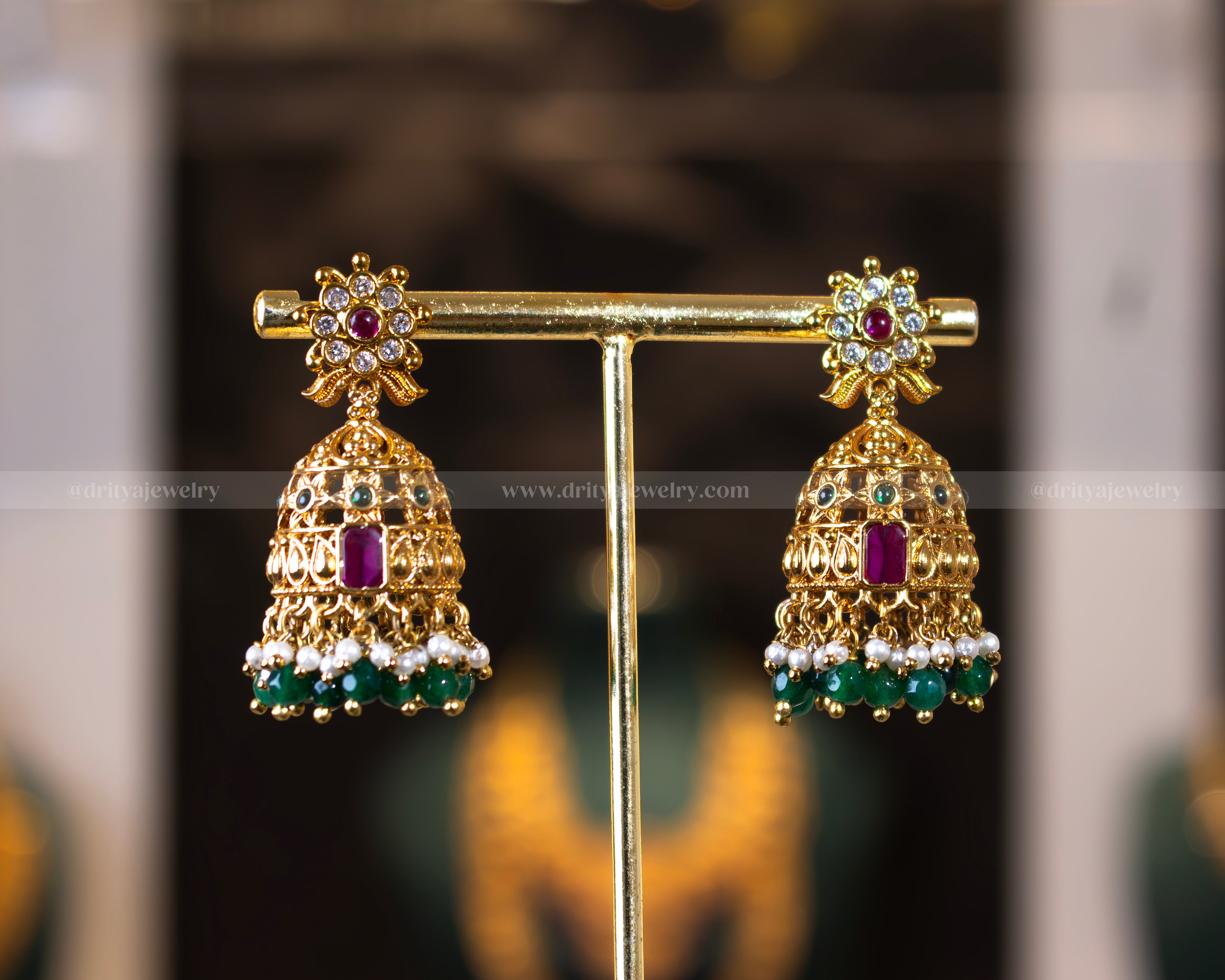 Close-up of Dritya Jewelry's temple-style jhumka earrings with green beads, designed with gold-plated temple motifs and colorful stones.