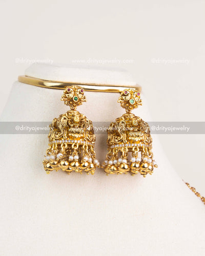 Gold temple jhumkas with Lakshmi motif, ruby-emerald detailing, and pearl hangings.