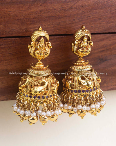 Antique gold jhumkas with Lakshmi motif, pearl clusters, and purple stone band.