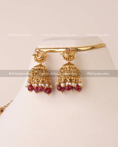 Gold Nakshi jhumkas with goddess carvings and ruby bead drops.